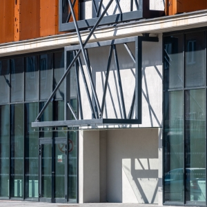 Architektonický detail antracitové ocelové konstrukce vstupního přístřešku na fasádě parkovacího domu s odleskem stínů.